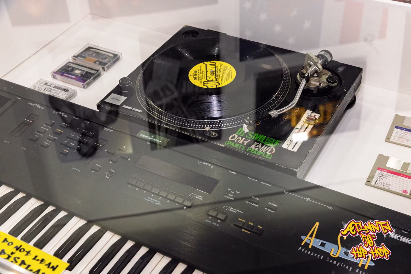 A turntable and keyboard preserved in a glass display case.