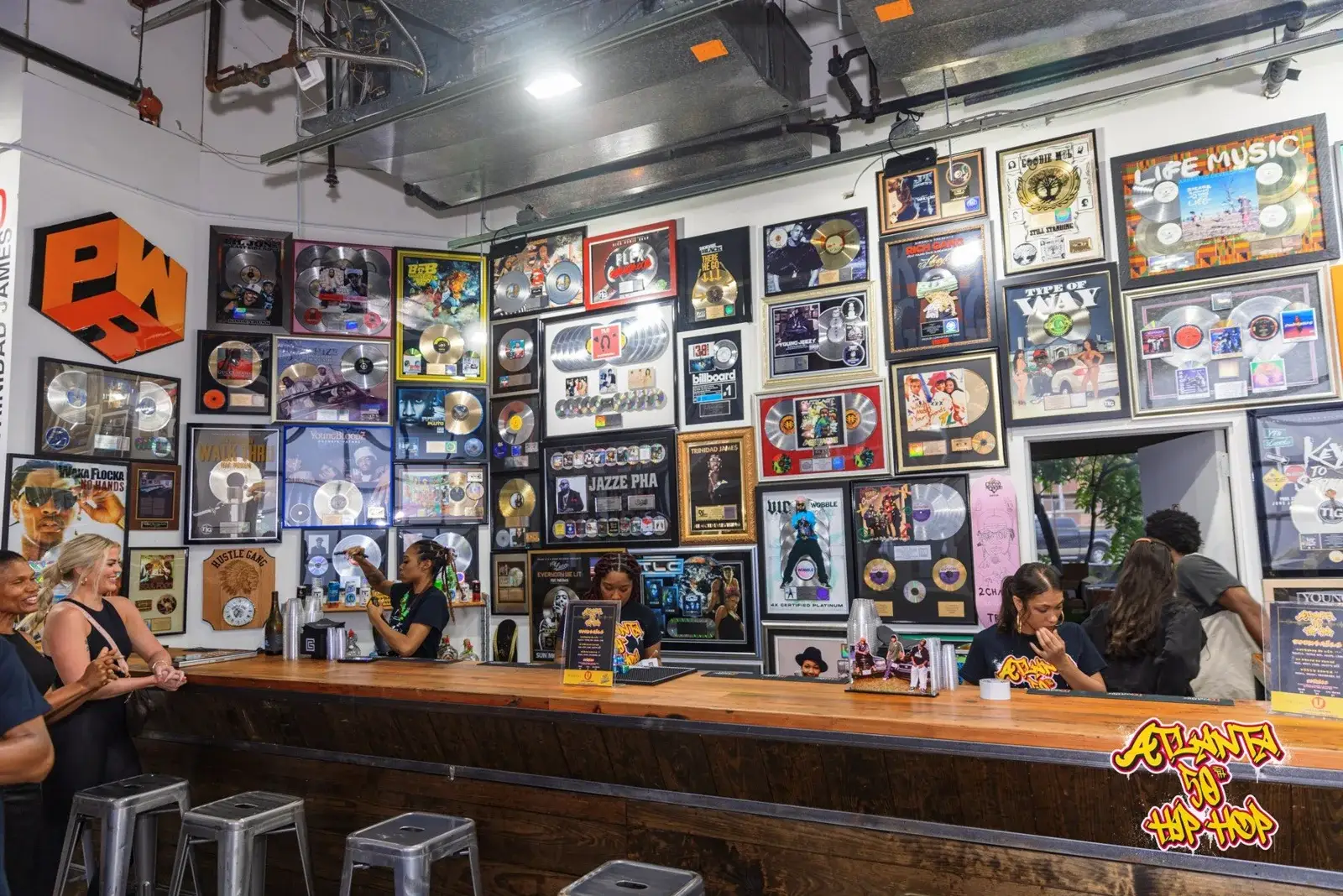 Visitors gather at a wooden bar beneath a wall of framed record awards.